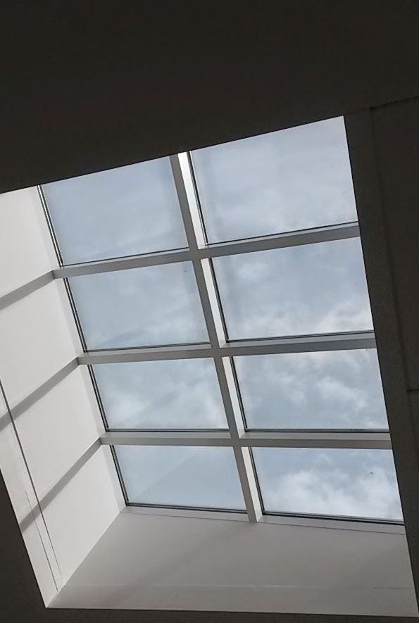 Lichtkuppel; Quelle: Astrid Anders Dachfenster mit Gitterstruktur und bewölktem Himmel im Hintergrund.